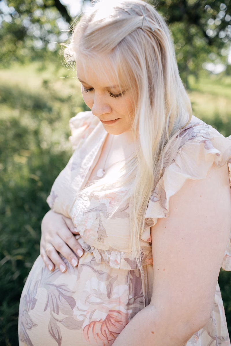 Schwangere Frau im romantischen Blumenkleid blickt liebevoll auf ihren Babybauch – Babybauch Bilder Vavrova Photography Göppingen