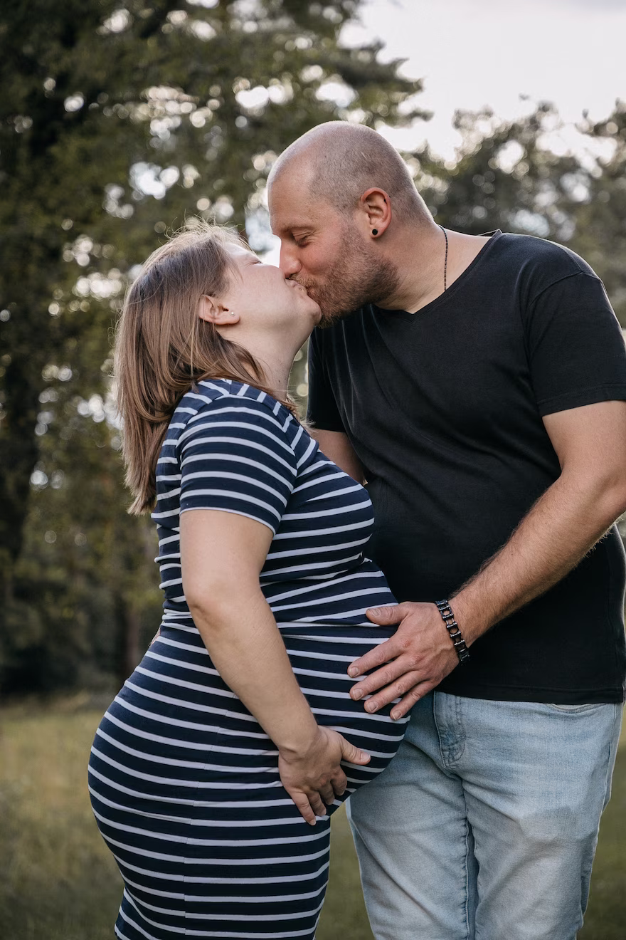 Schwangeres Paar küsst sich zärtlich in der Natur, Mann berührt liebevoll den Babybauch – Babybauch Shooting Vavrova Photography Göppingen